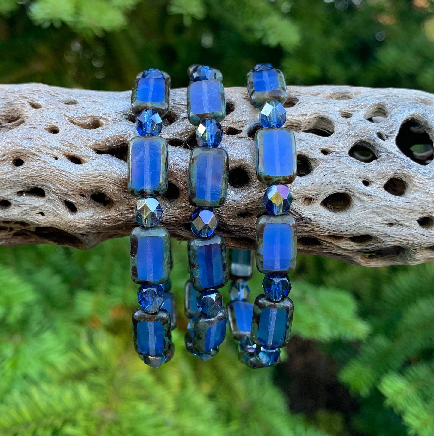 Blue beaded earrings on a piece of driftwood with a natural background