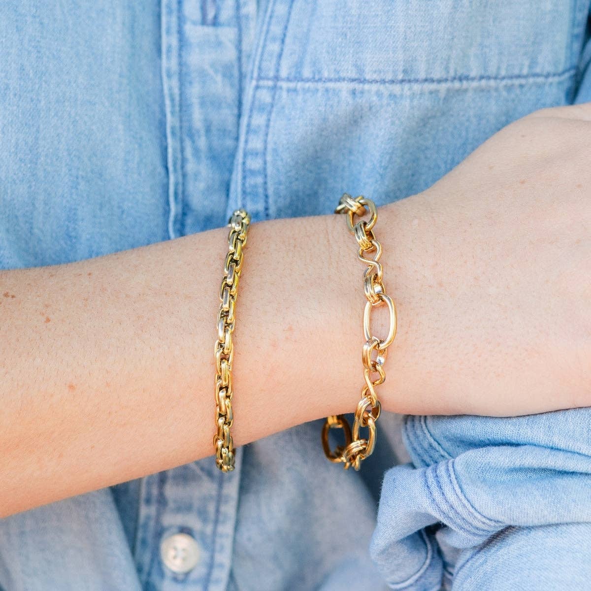 Gold chain bracelets on a person's wrist with a light blue denim shirt background