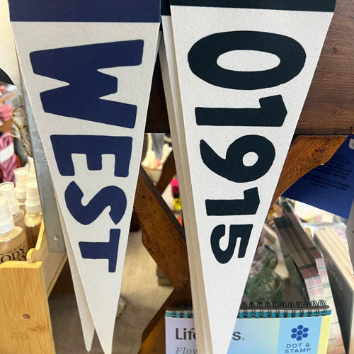 Two white hanging pennant banners with navy lettering, one reading "WEST" and the other "01915," attached to Benoit's Biscuit Co. cardboard hangers in a retail setting.