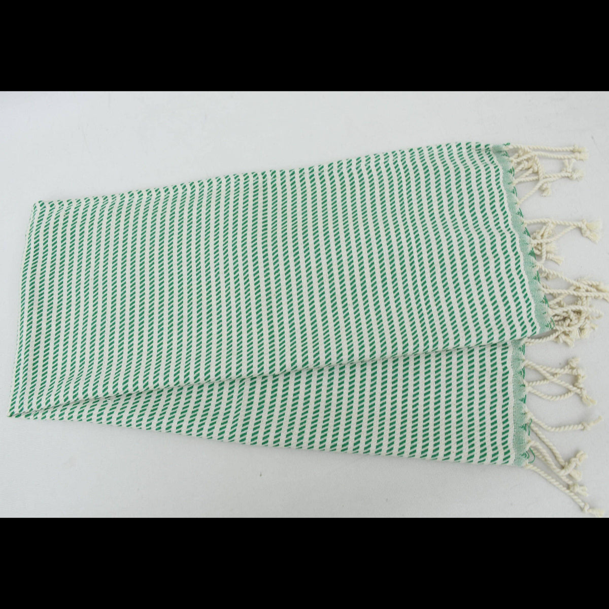 A folded Turkish cotton washcloth with a green and white wavy stripe pattern and cream-colored fringed tassels on one end, displayed on a plain white background.