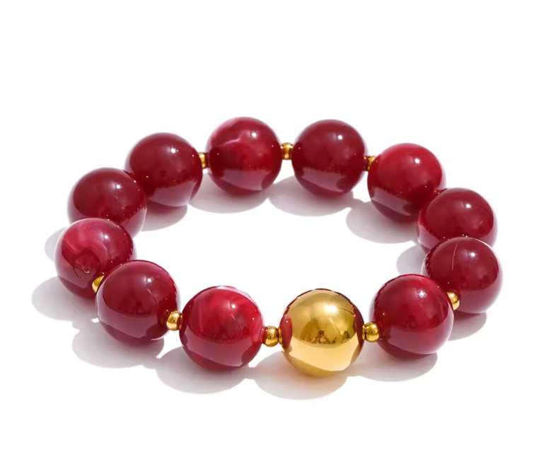 A beaded stretch bracelet featuring glossy deep red gemstone-like beads and one prominent shiny gold metallic accent bead, displayed on a clean white background.