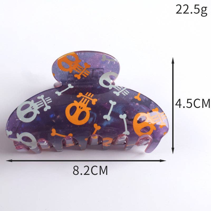 A claw hair clip with a purple glittery base decorated with orange and white skull and crossbones patterns, shown with dimension lines and text indicating measurements of 8.2cm width, 4.