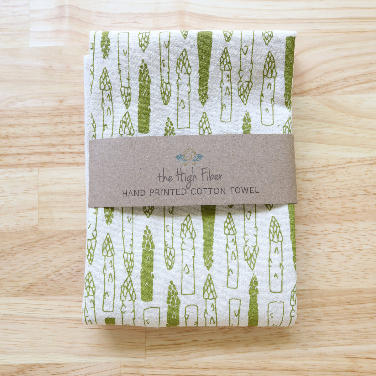 Folded hand-printed cotton towel with asparagus pattern on a wooden surface