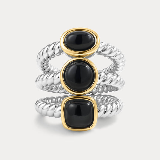 Three stacked rings with black gemstones and gold and silver bands on a light gray background