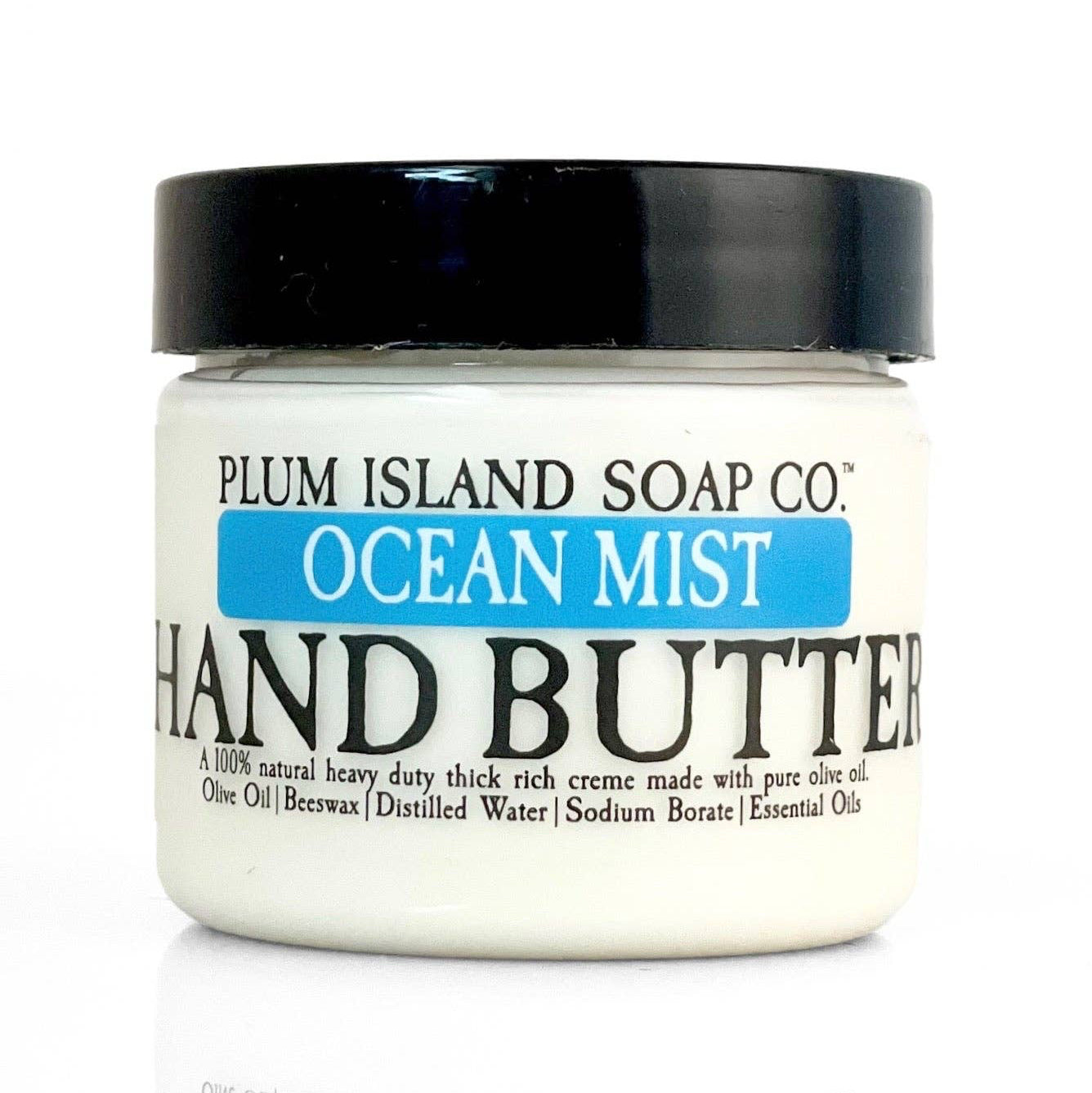 A jar of Plum Island Soap Co. Ocean Mist Hand Butter with an off-white body, black lid, and blue and black label text, shown on a white background with a reflection below.