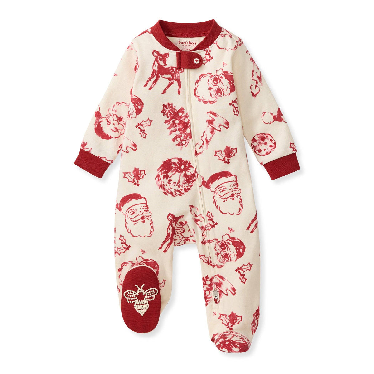 A baby footed sleeper in cream with a red Christmas print featuring Santa Claus, reindeer, pine trees, and holly, with red cuffs and a red snap closure at the neck.