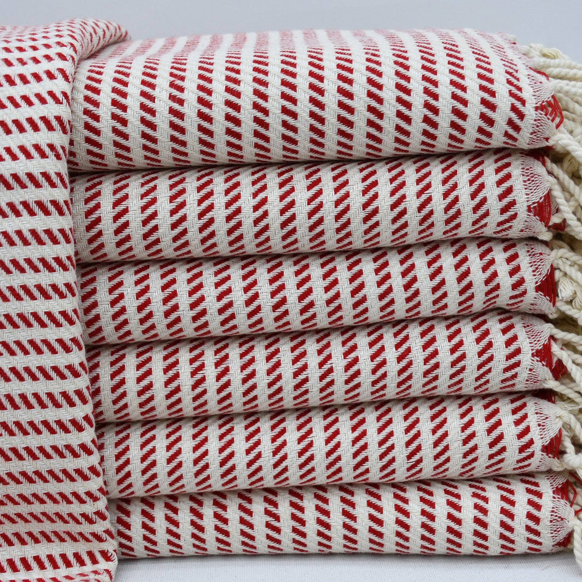A stack of folded Turkish cotton towels with red and white diagonal stripes and cream-colored fringed edges, displayed on a light gray background.