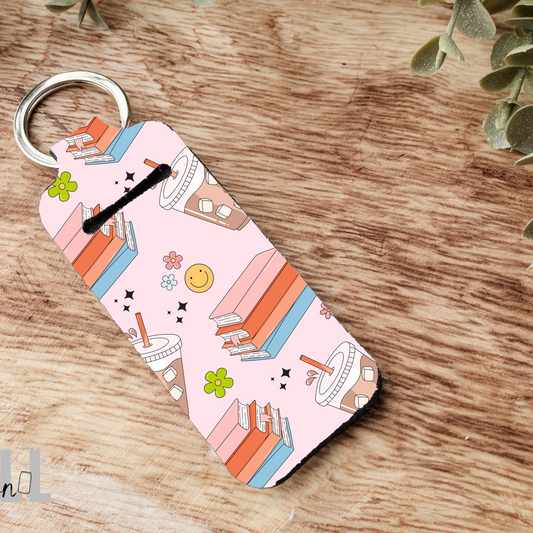 Keychain with a pink design featuring books and a coffee cup on a wooden surface.