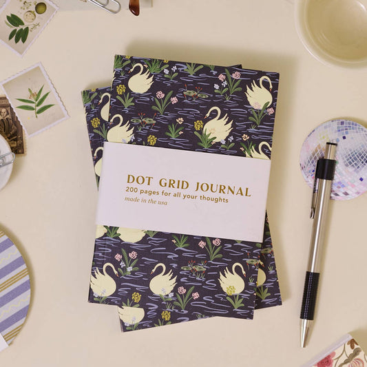 Dot grid journal with swan design on a desk with stationery items