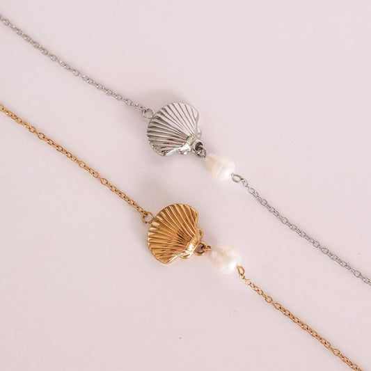Two delicate chain necklaces with scallop shell charms and small white pearls, one in silver and one in rose gold, displayed on a light pink background.