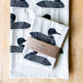Set of tea towels with loon designs on a wooden surface