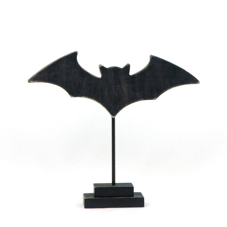 A black bat-shaped decorative plaque mounted on a thin vertical stand with a rectangular base, photographed against a plain white background.