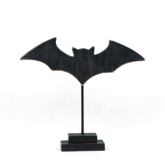 A black bat-shaped decorative plaque mounted on a thin vertical stand with a rectangular base, photographed against a plain white background.