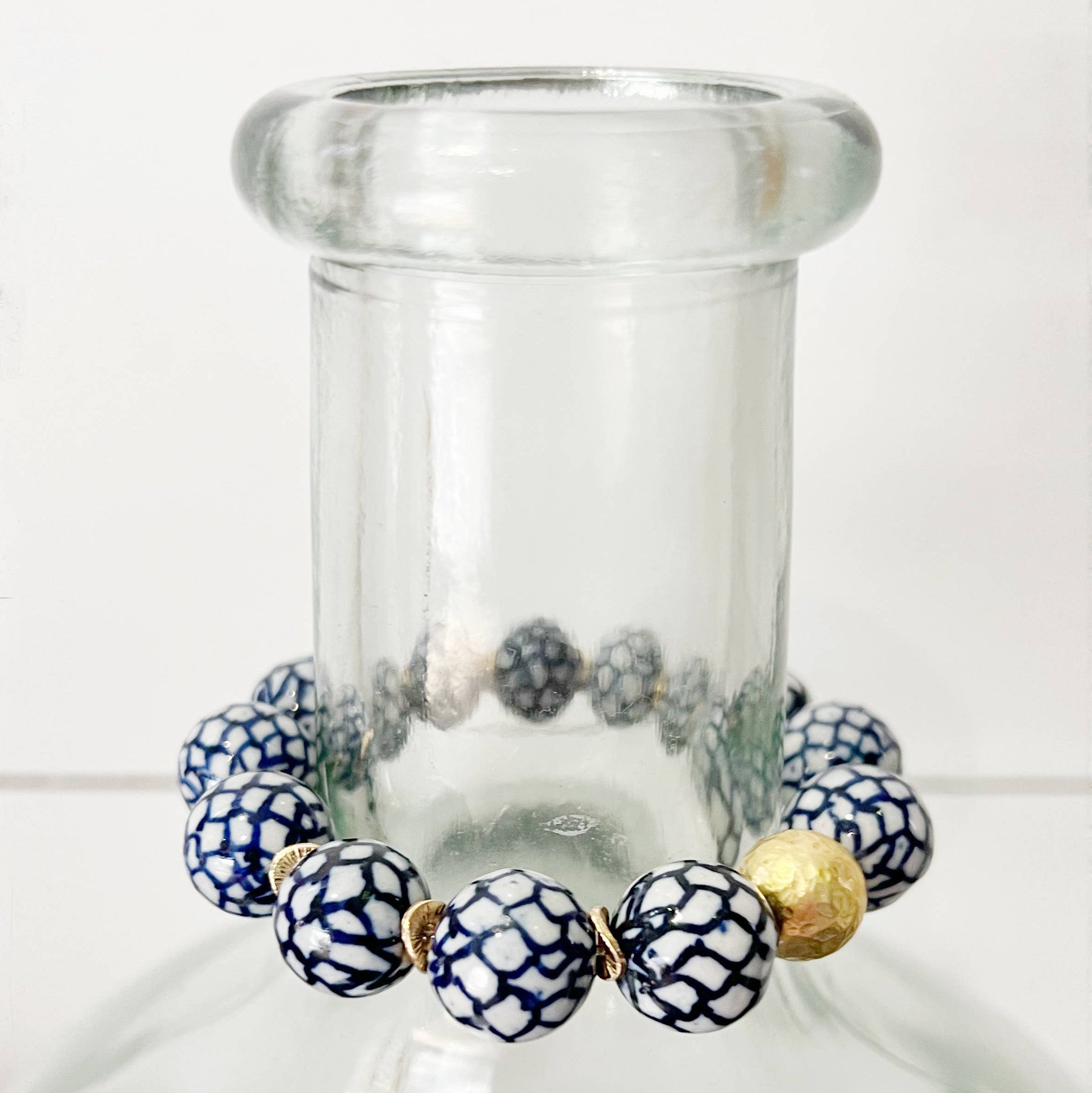 Bracelet with blue and white patterned beads and a gold bead on a clear glass bottle.