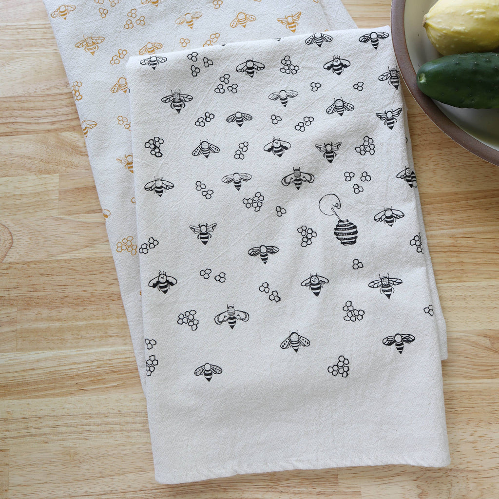 Two patterned towels on a wooden surface with kitchen items in the background.