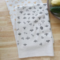Two patterned towels on a wooden surface with kitchen items in the background.