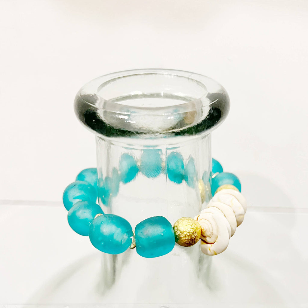 Turquoise beaded bracelet with gold and white accents on a clear stand against a white background