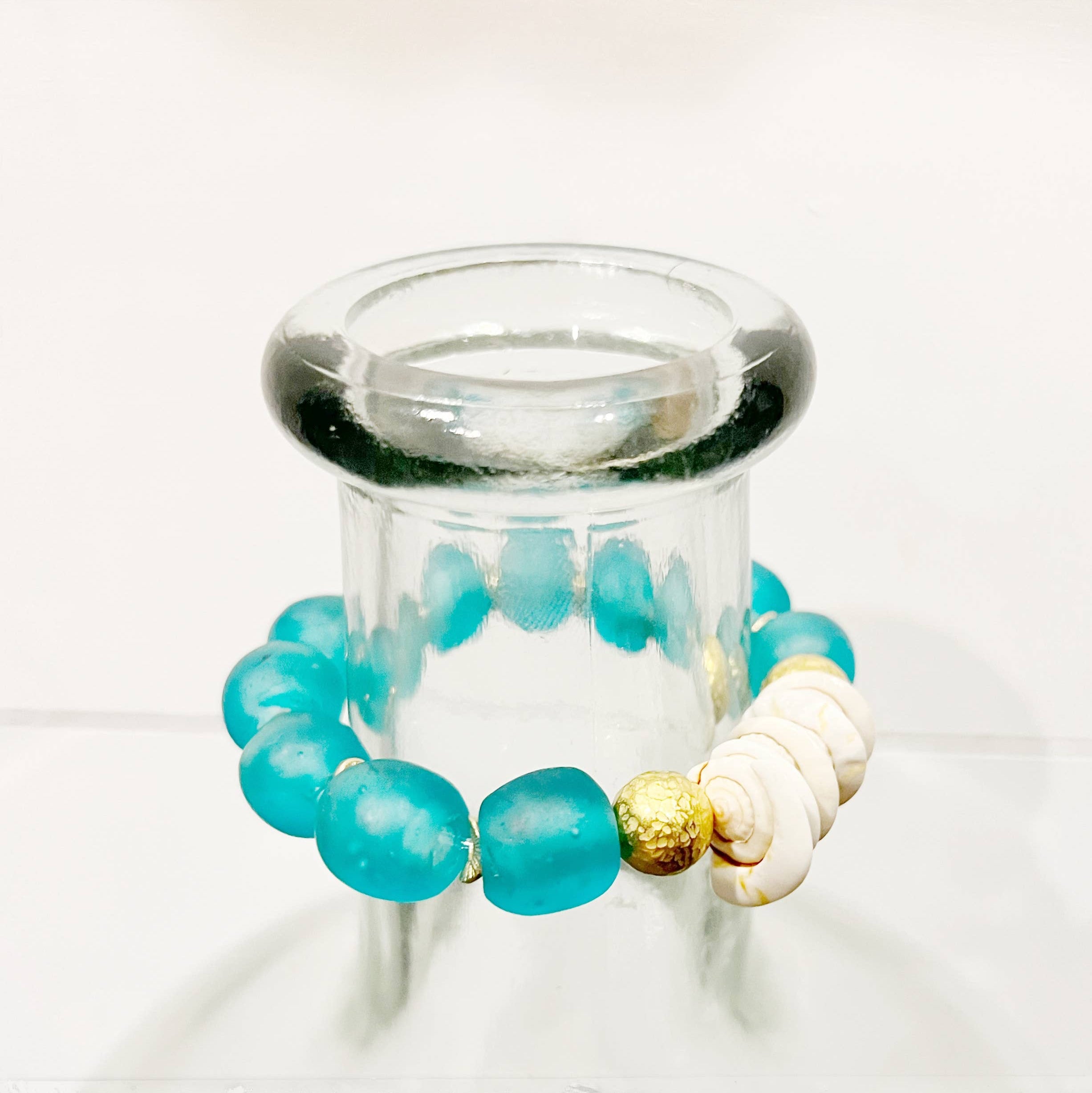 Turquoise beaded bracelet with gold and white accents on a clear stand against a white background