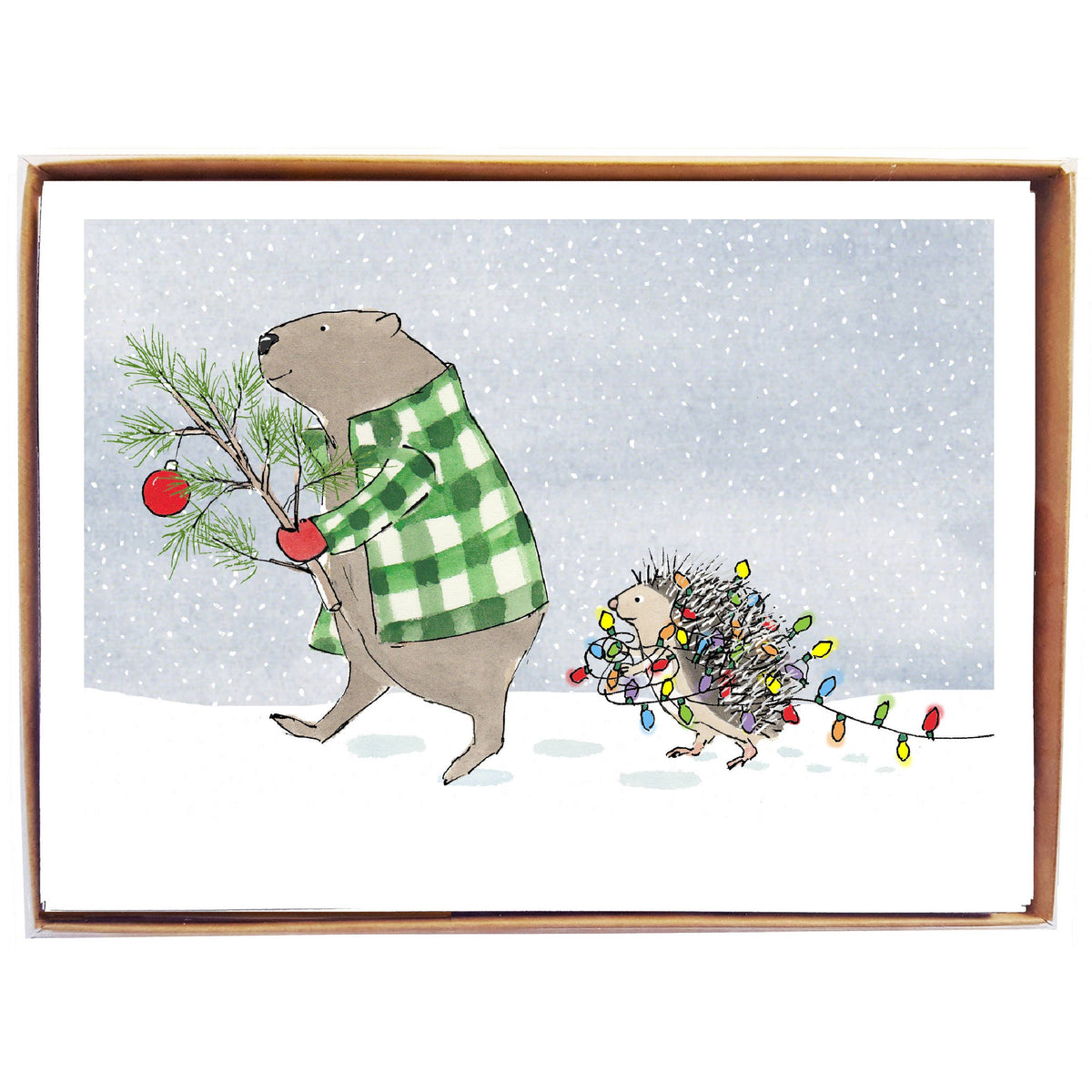 A square framed art print featuring a winter illustration of a beaver in a green-and-white plaid shirt carrying a pine branch with a red ornament, while a hedgehog wrapped in multicolored Christmas lights follows in the snowy scene.