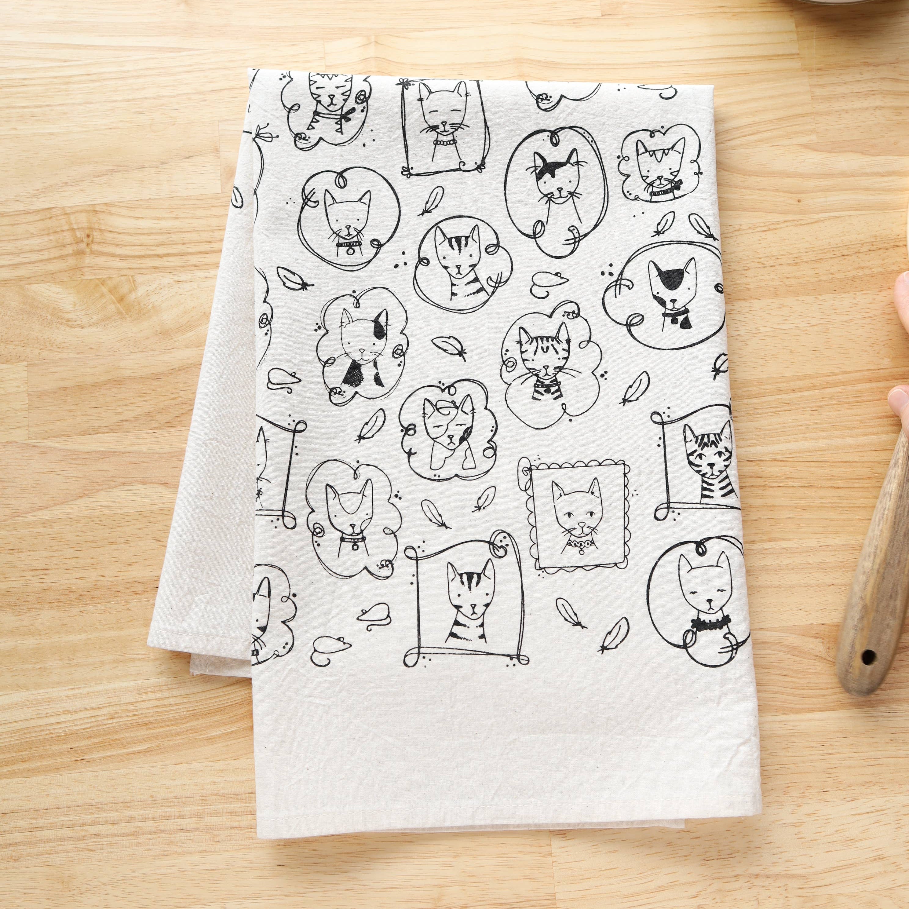 White towel with black cat illustrations on a wooden surface