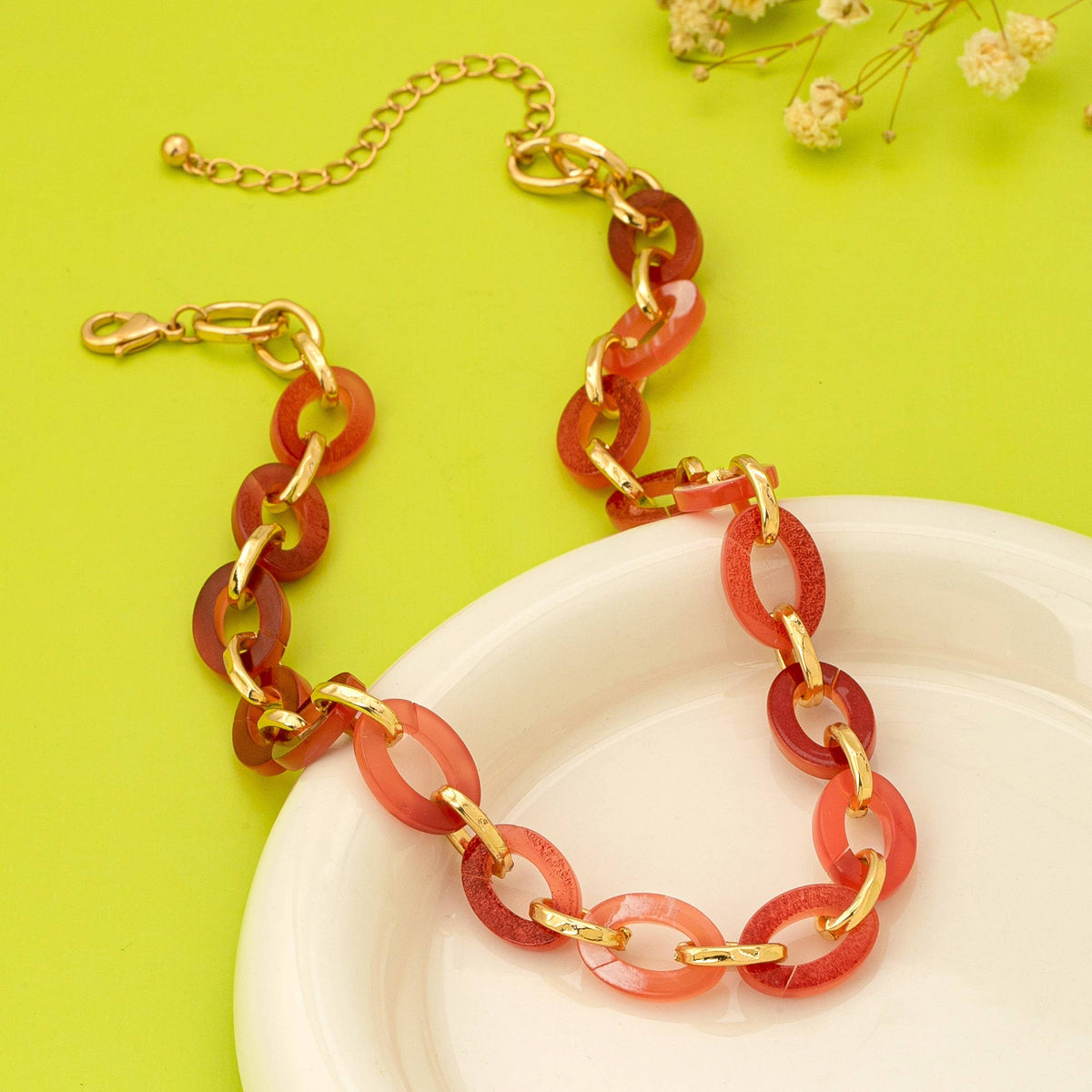 Necklace with red and gold chain on a white plate against a green background
