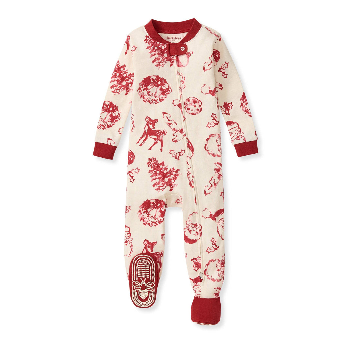 A baby footed sleeper in cream with a red holiday-themed print of reindeer, pine trees, ornaments, and snowflakes, featuring red ribbed cuffs and collar.