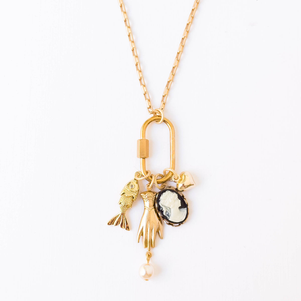 A gold-tone charm necklace featuring a lobster clasp pendant with a fish, a hand, a cameo-style oval medallion, and a dangling pearl bead, shown on a plain white background.