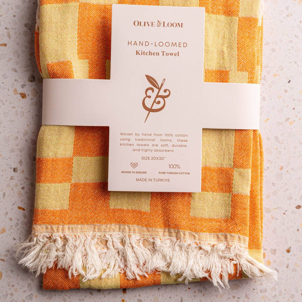 Checkered hand-loomed kitchen towel with a label on a textured surface
