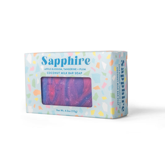 Sapphire Coconut Milk Bar Soap in a light blue box with multicolored confetti patterns and a clear window showing the purple and pink marbled soap inside.
