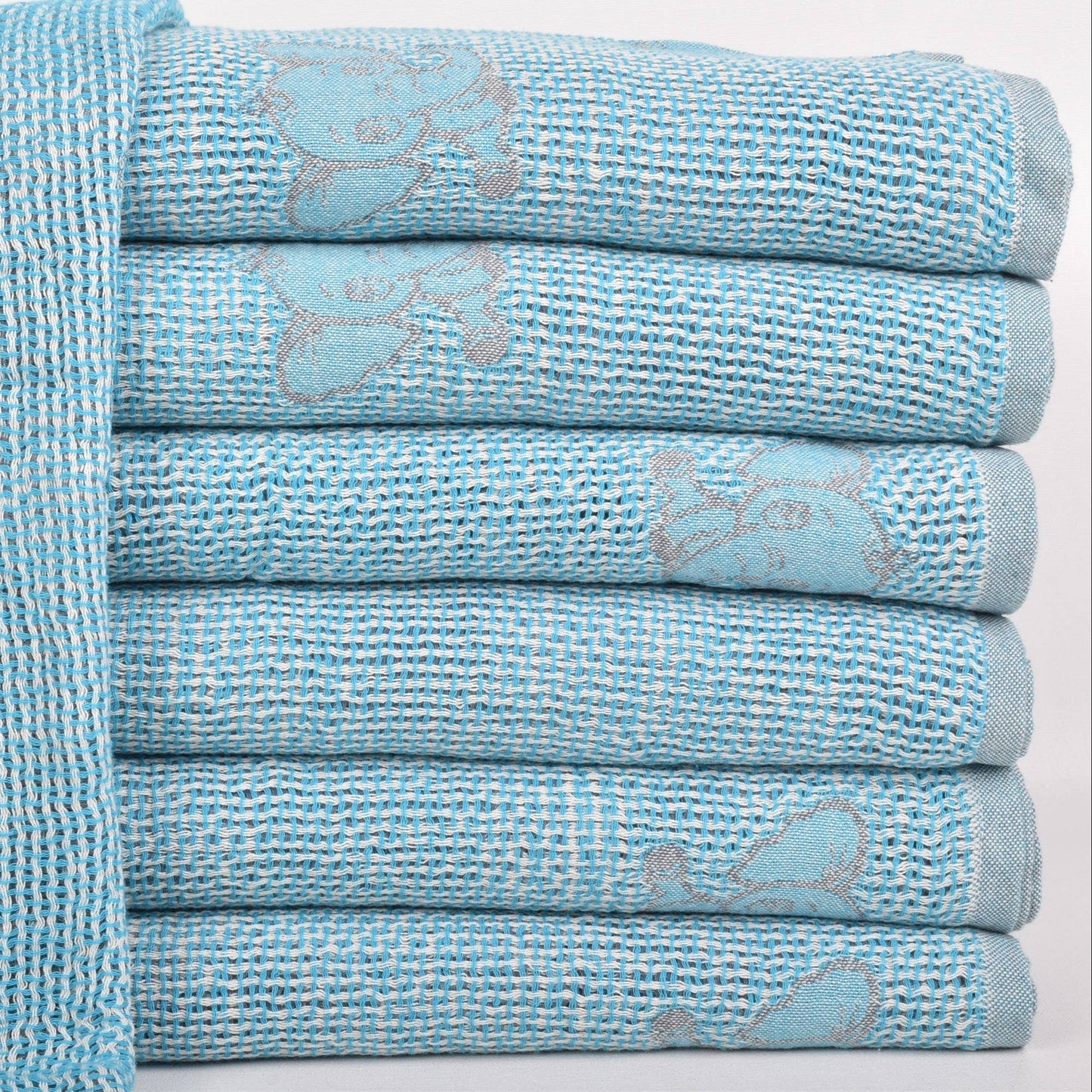 A stack of light blue textured towels with a subtle elephant pattern, with one towel laid flat on the left showing the design more clearly.
