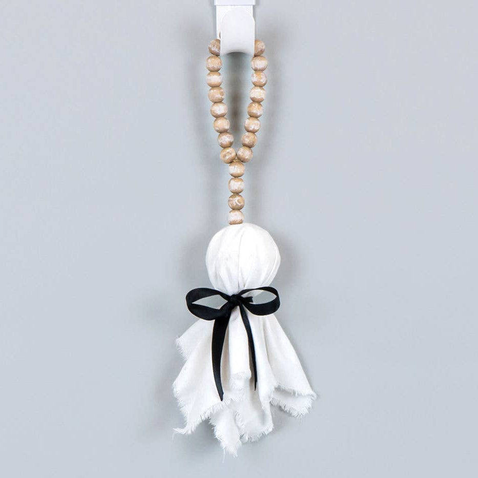 A hanging Halloween decoration featuring a white gauze ghost with a black ribbon bow and a string of wooden beads at the top, shown against a plain light gray background.
