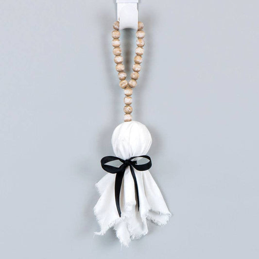 A hanging Halloween decoration featuring a white gauze ghost with a black ribbon bow and a string of wooden beads at the top, shown against a plain light gray background.