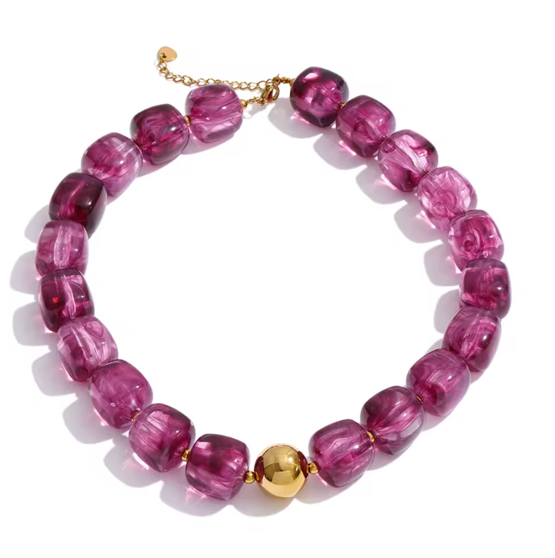 A beaded necklace featuring translucent magenta-pink glass beads with a polished gold accent bead and gold-toned chain clasp, shown on a white background.