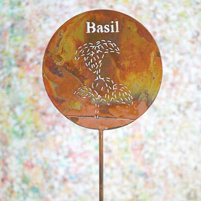 Decorative garden stake with 'Basil' text and leaf design on a colorful blurred background