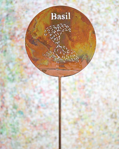 Decorative garden stake with 'Basil' text and leaf design on a colorful blurred background