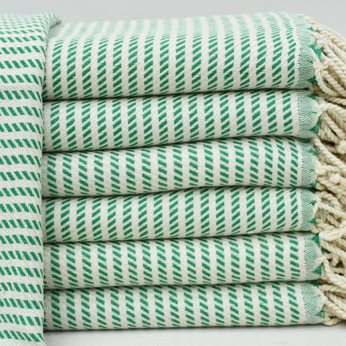 A stack of folded cotton towels with a green and white diagonal striped pattern and cream-colored fringed edges, shown on a light background.
