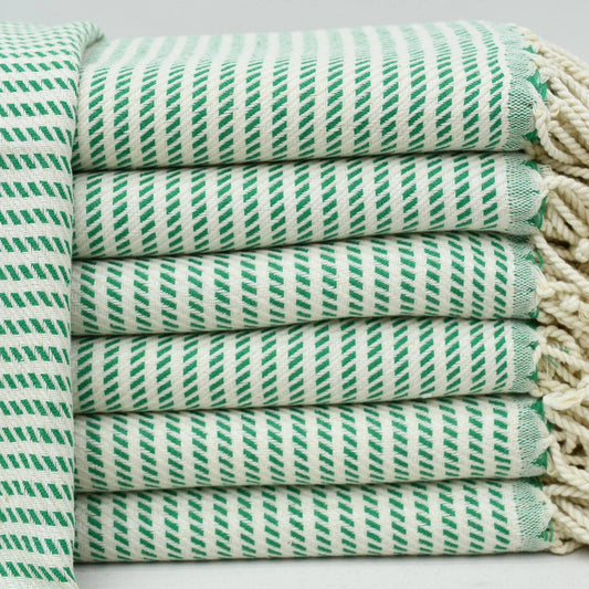 A stack of folded cotton towels with a green and white diagonal striped pattern and cream-colored fringed edges, shown on a light background.