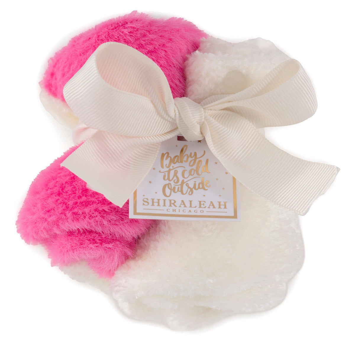 A pair of fluffy baby booties in bright pink and white, tied together with a large cream ribbon bow and a gold tag that reads 'Baby it's cold Outside Outside SHIRALEAH'.