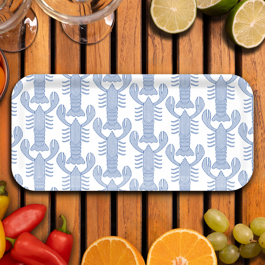 Rectangular plate with blue lobster pattern on a wooden surface with fruits and vegetables.