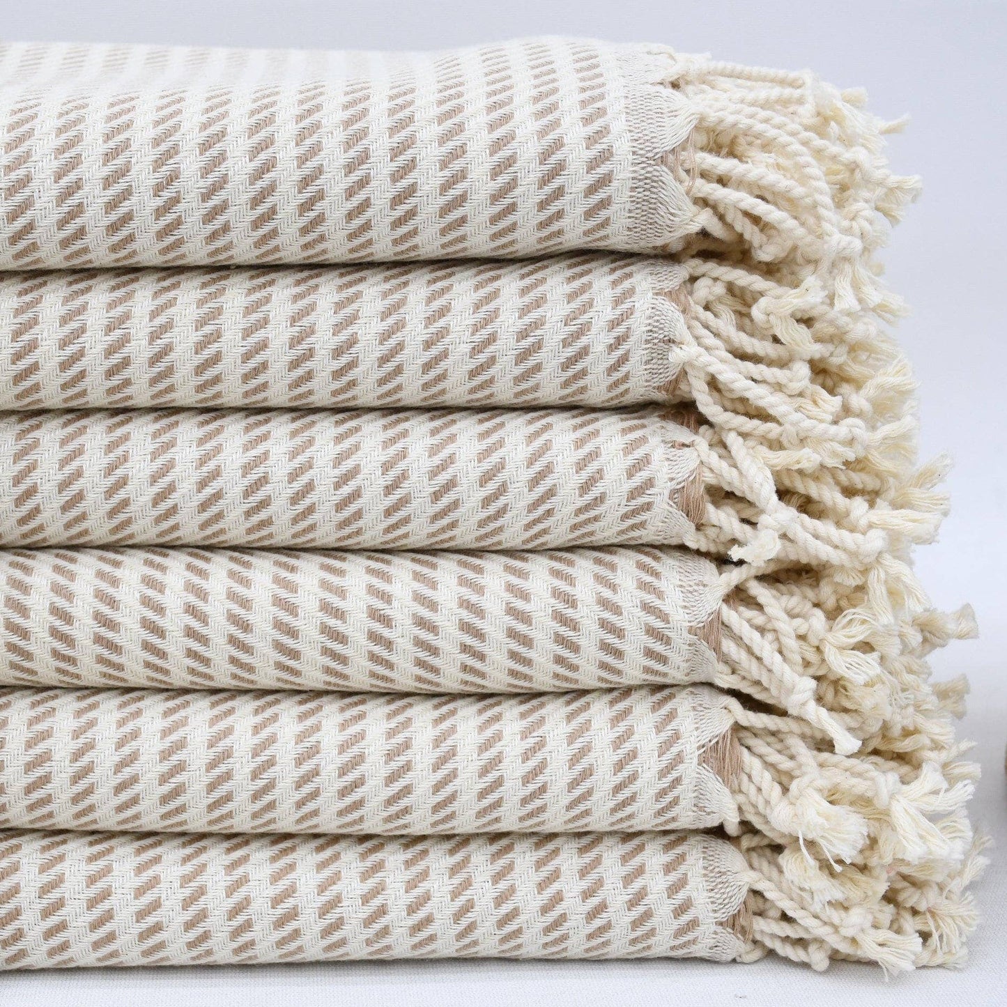 Stack of beige woven towels with tassels on a light background