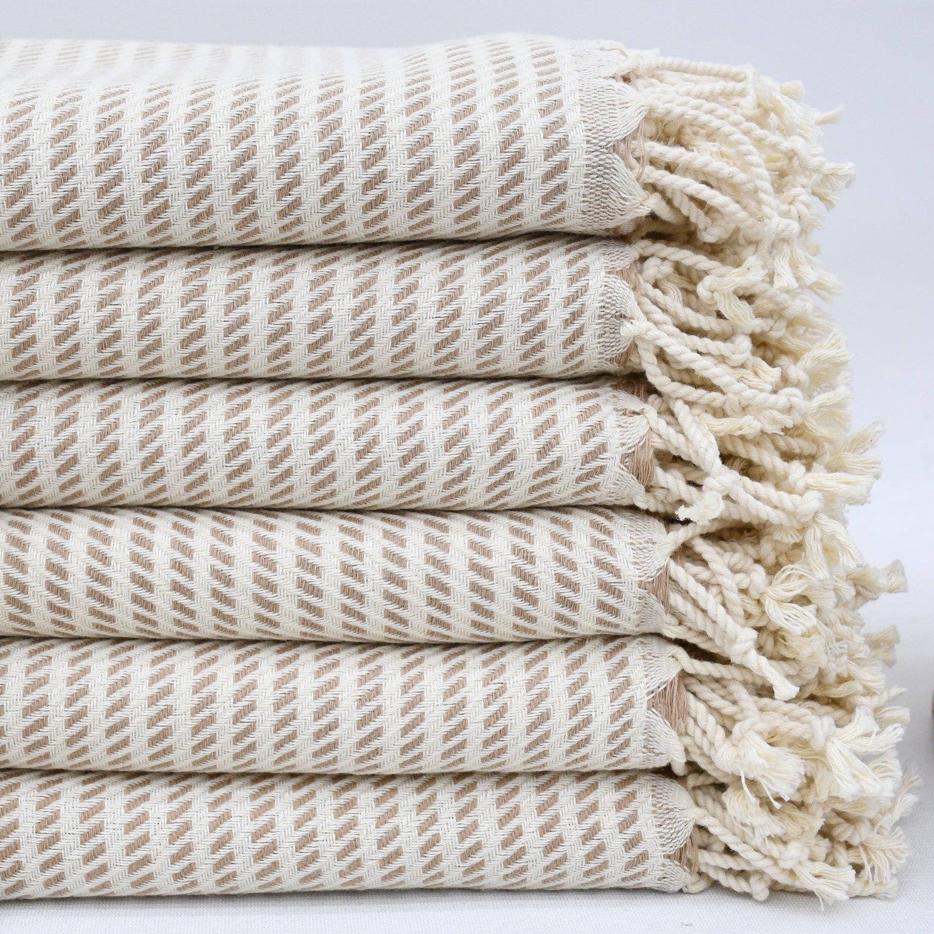 Stack of beige woven towels with tassels on a light background