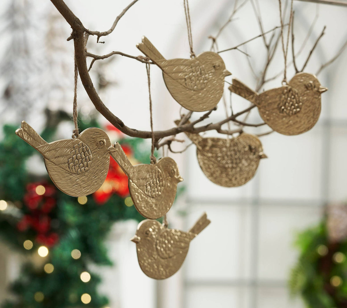 Gold bird-shaped ornaments hanging on a branch with a blurred Christmas tree in the background.