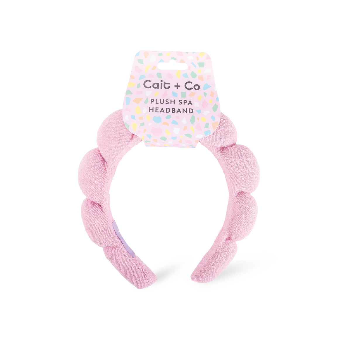 A pink plush braided headband by Cait + Co, attached to its original printed cardboard hanger, shown against a plain white background.