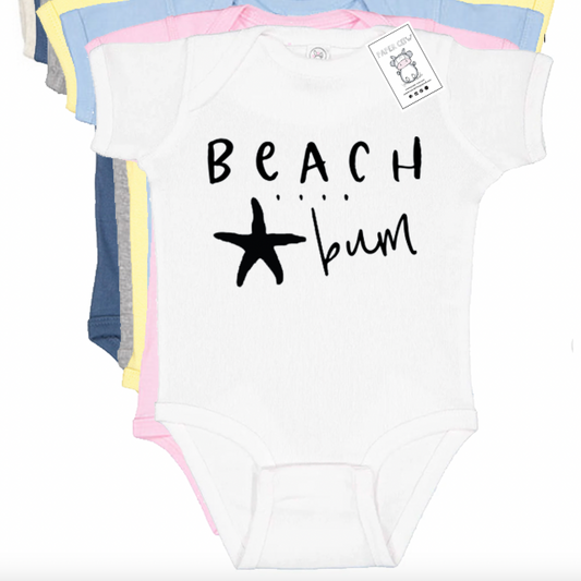 A stack of baby short-sleeve bodysuits in white, navy, gray, yellow, and pink, with the front white bodysuit featuring the black text 'BEACH .