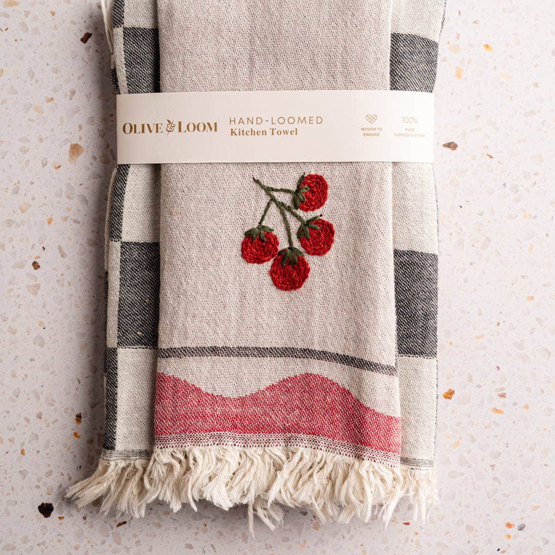 Hand-loomed kitchen towel with cherry design and Olive & Loom branding on a textured surface.