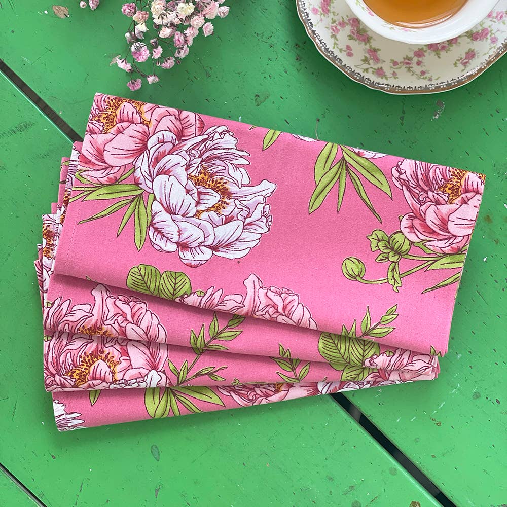 Folded pink floral fabric on a green surface with a cup of tea in the background